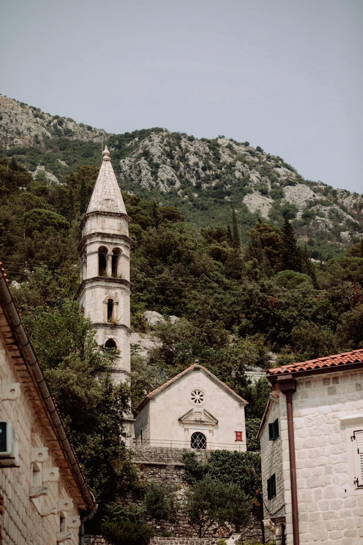 Alter Kirchturm in mediterranem Dorf vor bewaldeten Bergen
