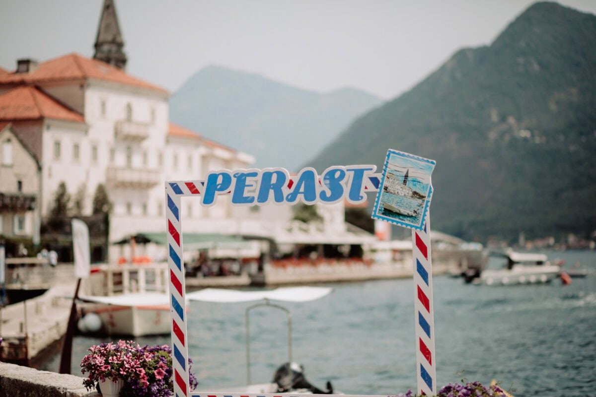 Perast Schild am Hafen mit Bergen und Altstadt im Hintergrund
