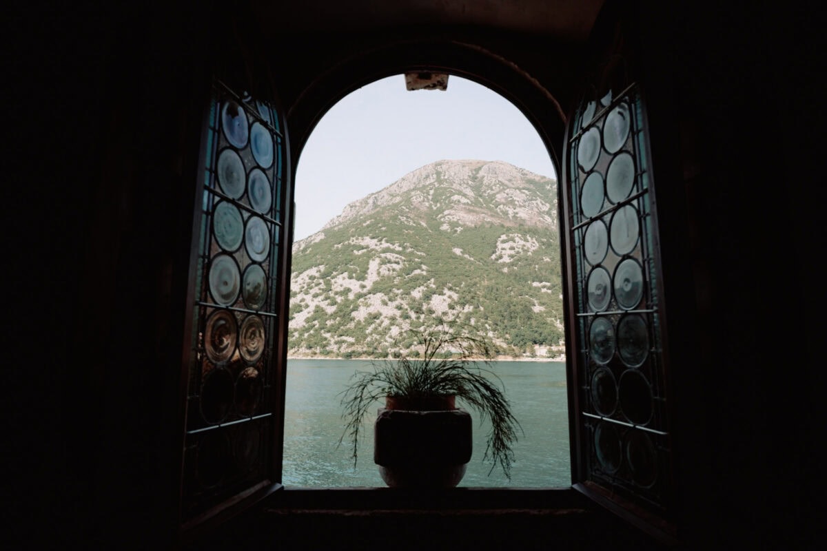 Bogenfenster mit Buntglas, Blick auf See und Berg